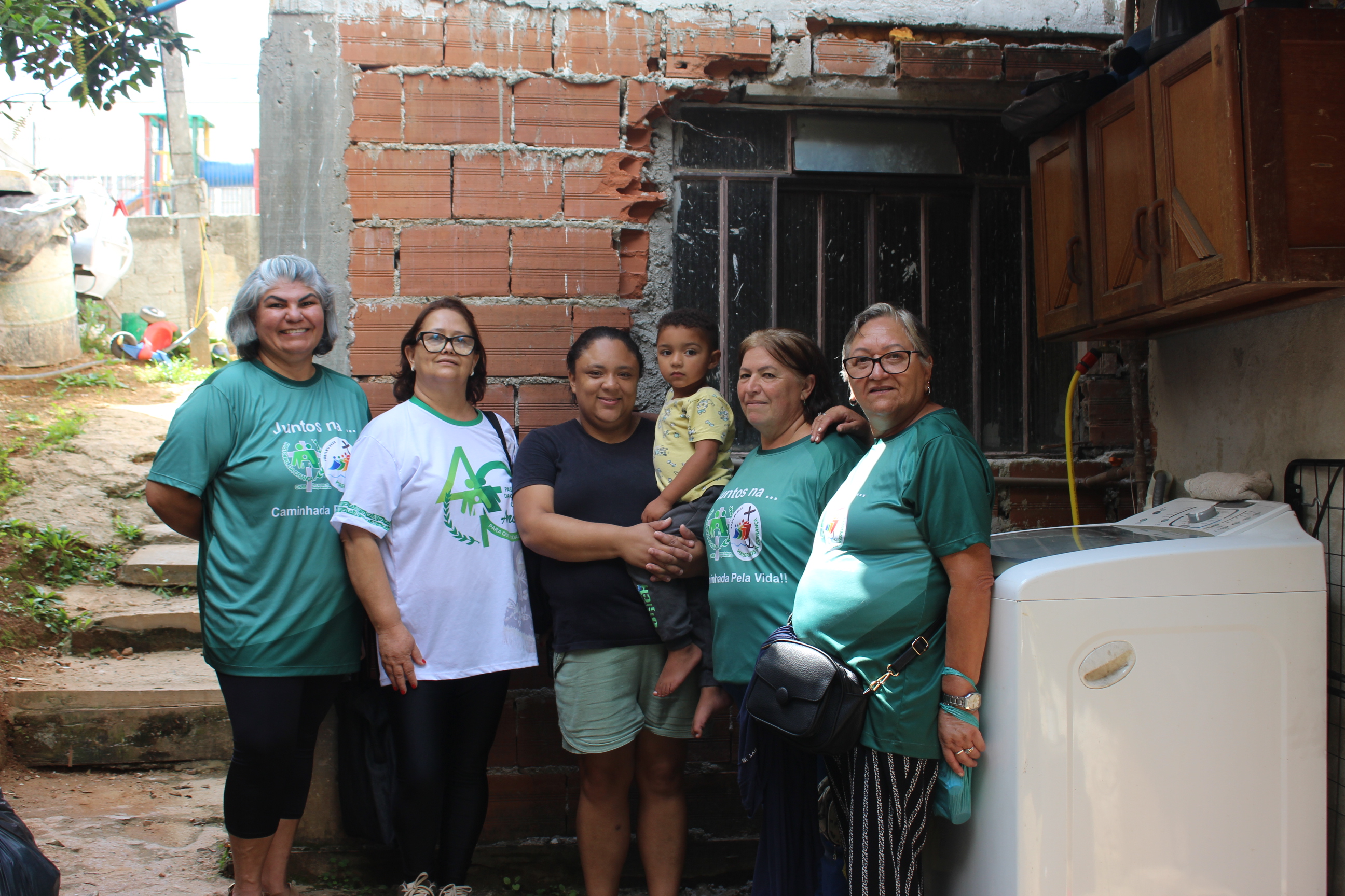 L&iacute;deres da Pastoral da Crian&ccedil;a reunidas em uma casa com uma m&atilde;e e uma crian&ccedil;a pequena, todos sorrindo