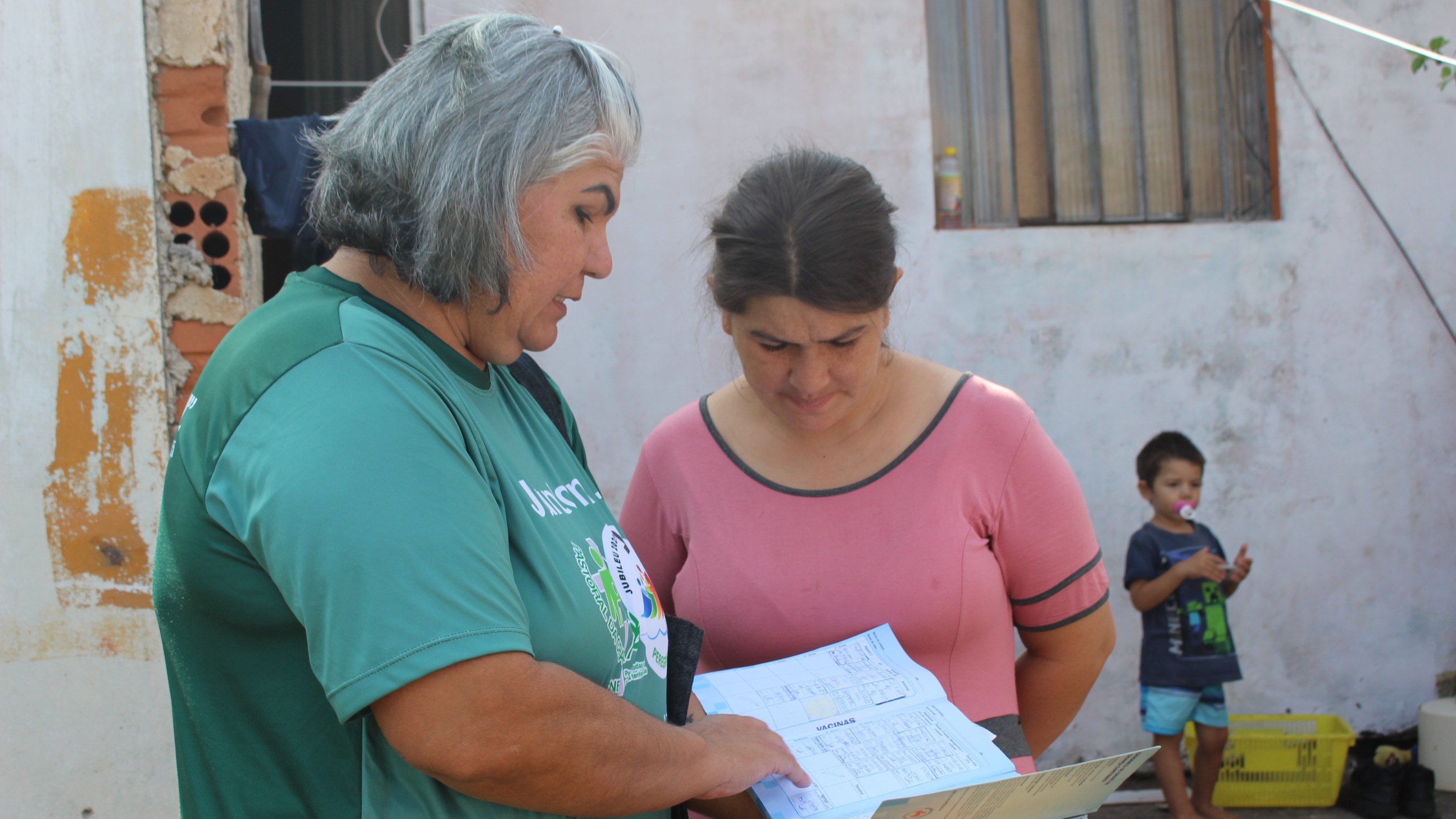 Líder da Pastoral da Criança observando a caderneta de vacinação durante visita domiciliar